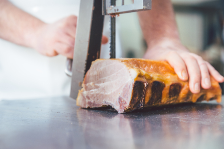 Butcher cutting meat in butchery with sawの写真素材