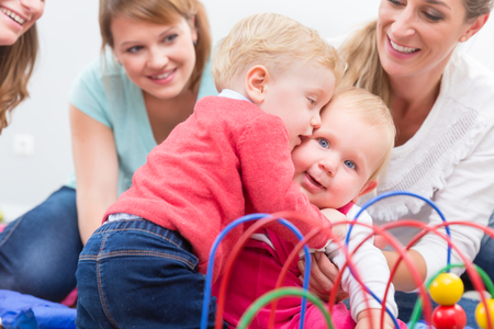 Group of happy young mothers watching their cute and healthy babies while playing with multicolored toys in a modern daycare centerの写真素材