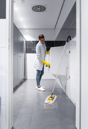 Janitor woman cleaning urinals in public mens toiletの写真素材