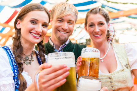 Three friends at Bavarian folk fair clinking beer glasses in tentの写真素材