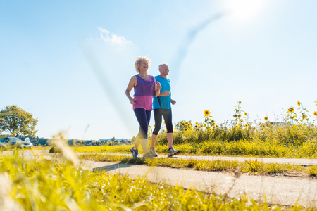 Full length rear view of two healthy senior people jogging on a country road against clear blue sky in summerの写真素材