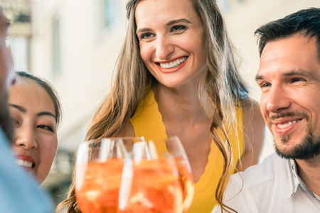 Beautiful woman and her best friends toasting with a refreshing alcoholic drink while sitting together at table outdoors in a trendy restaurant in summerの写真素材