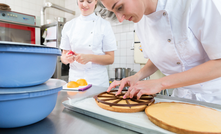 Patissier women working on fruit cake putting apple slices on themの写真素材