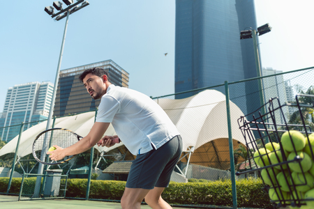 Low-angle view of a young handsome man ready to serve while playing tennis outdoors in a modern district of the cityの写真素材