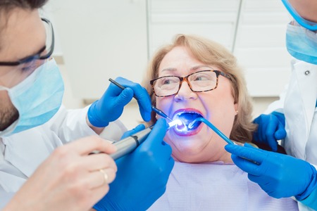 Dentists hardening toot crown with UV light treating senior patientの写真素材