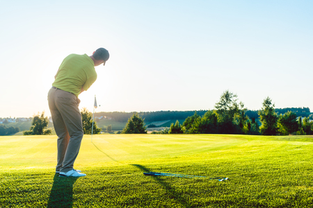 Full length rear view of an experienced male golfer hitting the golf ball towards the cup on the putting green, during a professional individual game in summerの写真素材