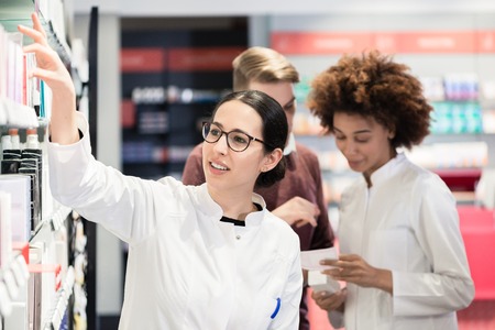 Portrait of a female experienced pharmacist reading the indications from the package of a new pharmaceutical product during work in a contemporary drugstoreの写真素材