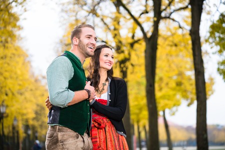 Man and woman wearing Bavarian Tracht, in close position, standing in front of an alley in fallの写真素材