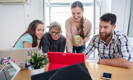 Four co-workers smiling, while watching together a professional business presentation or a funny...