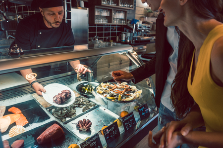 Experienced chef choosing raw seafood from the freezer for two customers in a trendy restaurant or cafeteria with fresh foodの写真素材
