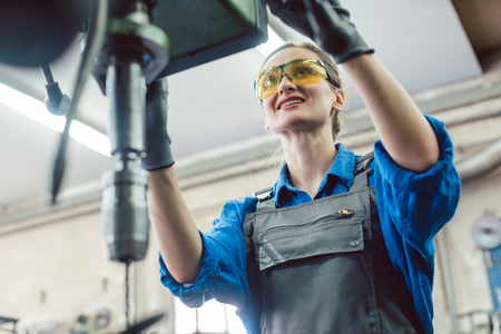 Woman worker in metal workshop using pedestal drill to work on pieceの写真素材