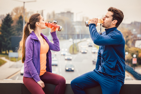 Woman and man drinking water in break from fitness training with a cityscape in the backgroundの写真素材