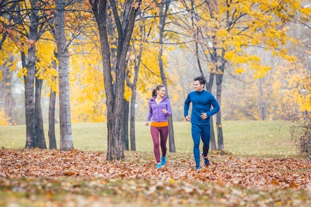 Woman and man running on a path in autumn park for sportの写真素材