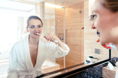Woman brushing her teeth in luxurious hotel bathroom looking at herself in mirrorの写真素材