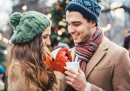 Woman and man drinking mulled wine on Christmas Market in front of treeの写真素材