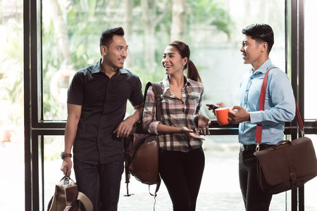 Three young and cheerful employees wearing trendy casual clothes while talking together in the...