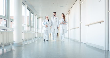 Doctors, two women and a man, in hospital walking down the corridorの写真素材