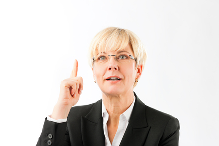 Smiling mature businesswoman wearing eyeglasses pointing finger upward isolated over white backgroundの写真素材