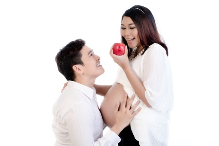 Smiling man looking at his pregnant wife holding red apple in her hand
