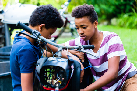 Boys looking at vintage motorbike in the gardenの写真素材
