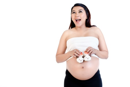 Close-up of excited pregnant woman holding pair of baby shoes over her belly