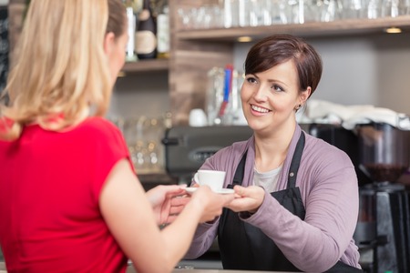 Female waitress giving small coffee cup to the woman in cafeの写真素材