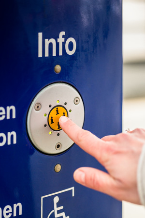 Woman pressing info button of assistance machine in train station, only finger to be seenの写真素材