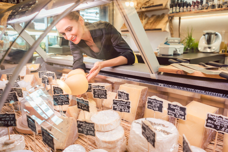 Shop clerk woman sorting cheese in the supermarket display to sell itの写真素材