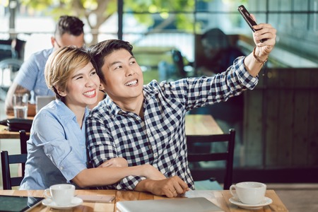 Portrait of young couple taking selfie in the cafe through cellphoneの写真素材