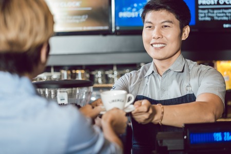 Portrait of young smiling barista serving coffee to female customer in the coffee shop