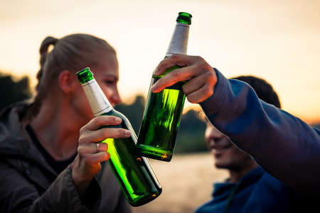 Close-up of couple clinking their beer bottles outdoorsの写真素材