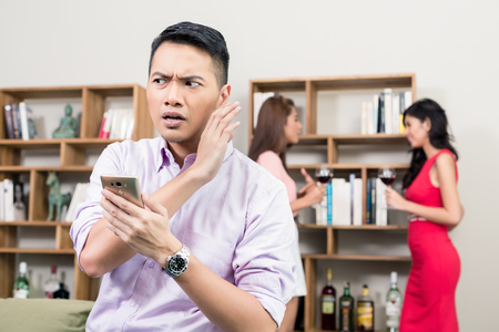 Close-up of a young man trying to secretly listen the conversation between two womenの写真素材