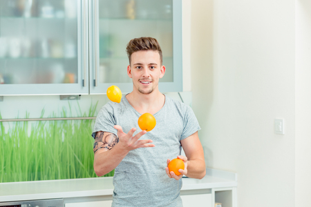Portrait of smiling young man juggling with fresh orangesの写真素材