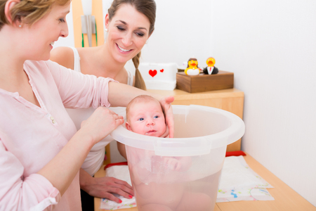 Smiling mother looking at woman holding baby in the bucket for bathingの写真素材