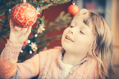 Young girl decorating the Christmas tree, holding some Christmas baubles in her hand being amazed by the festive atmosphereの写真素材