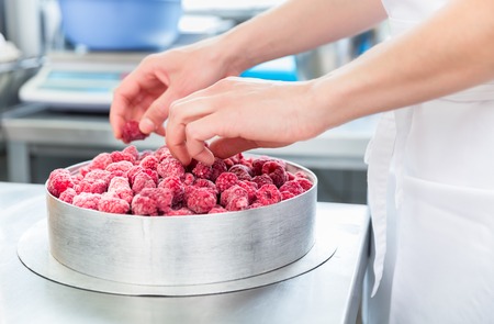 Woman confectioner making raspberry cake in bakeryの写真素材
