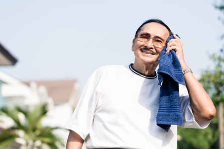 Happy elderly man wiping his sweat with blue napkin after doing exerciseの写真素材