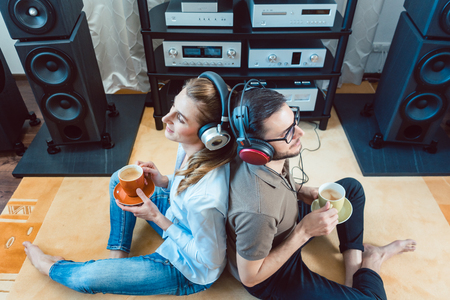 Couple with headphones enjoying music from the Hi-Fi stereo leaning at each otherの写真素材