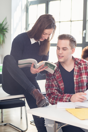 Two cheerful students checking and comparing information and knowledge while learning together in the classroom at college or universityの写真素材