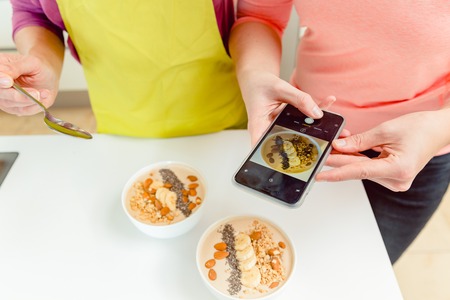 Female food blogger takes pic of healthy oatmeal bowls for blog through cellphoneの写真素材