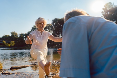 Full length of a funny senior couple playing with water at the river while enjoying their happy relationship in a sunny day of summerの写真素材