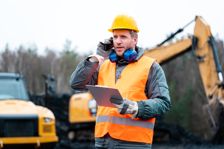 Portrait of a quarry worker standing in front of excavator smiling