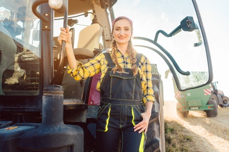 Farmer woman standing in front of tractor on wheat field on a sunny afternoonの写真素材