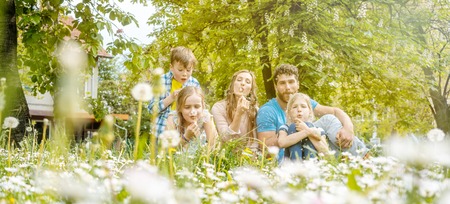 Family of five sitting on a meadow blowing dandelion flowers being happy and playful