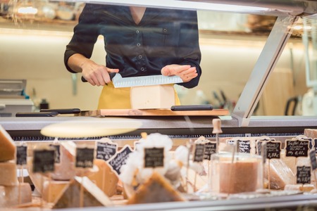 Shop clerk woman sorting cheese in the supermarket display to sell it