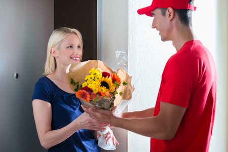 Smiling young female customer receiving beautiful flower bouquet from delivery manの写真素材