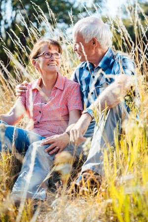 Couple of senior woman and man sitting in a meadow in the grass looking at each otherの写真素材