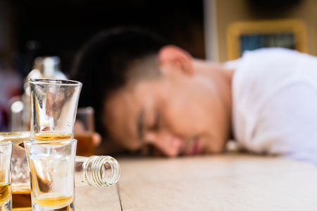 Hangover sleeping man behind the empty glasses and bottle on tableの写真素材