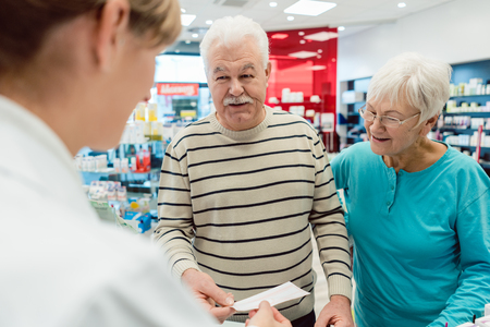 Pharmacist getting prescription slip from senior couple in her pharmacyの写真素材