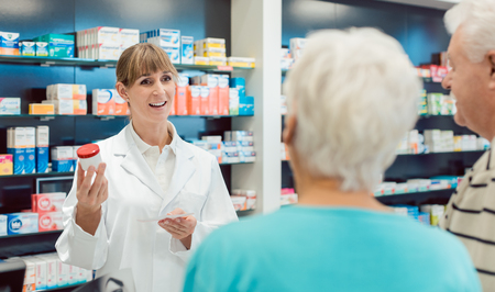 Chemist advising senior couple on a prescription drug in her pharmacyの写真素材
